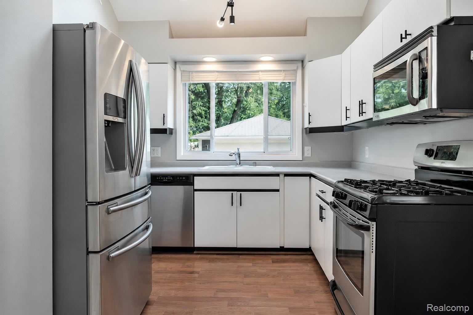 Kitchen featuring stainless steel appliances, white cabinetry with dark hardware, a gas range, wood-finish flooring, and a large window