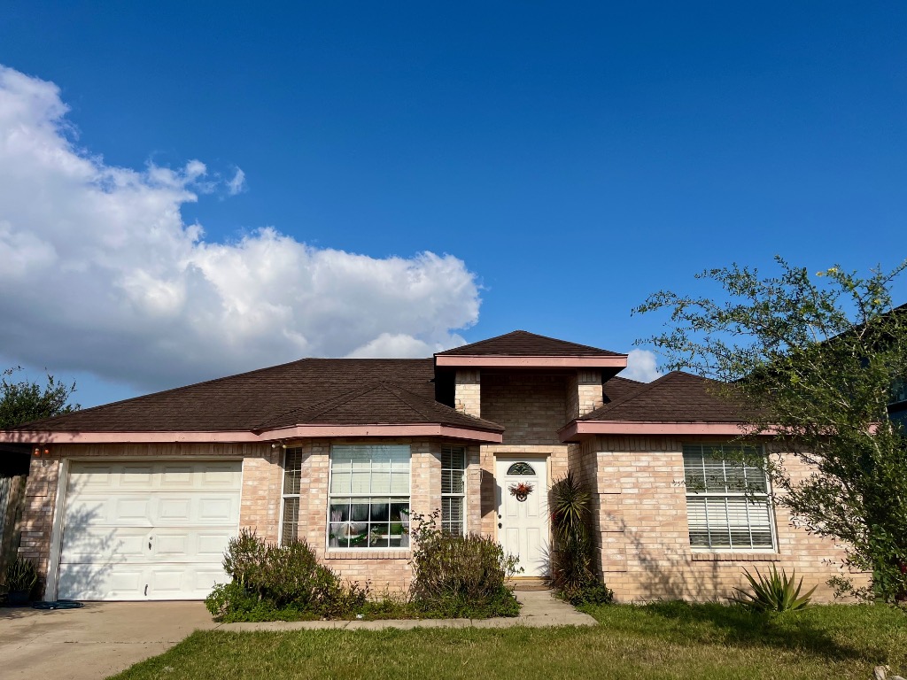 Ranch-style home featuring brick siding, an attached garage, driveway, a shingled roof, and a front lawn