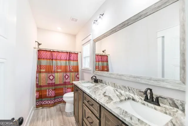 a bathroom with a granite countertop double vanity sink a mirror and shower