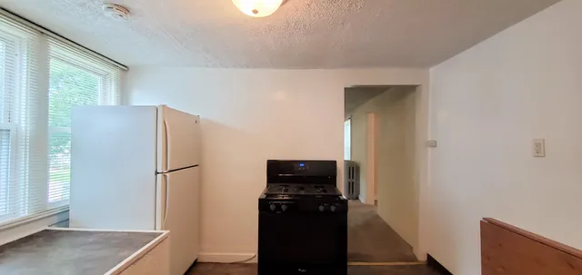 a view of a refrigerator in kitchen and an empty room with wooden floor windows