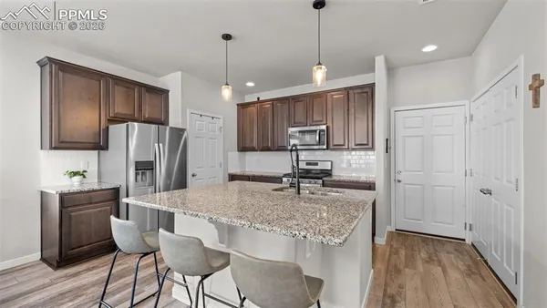 a kitchen with stainless steel appliances granite countertop a refrigerator a sink a stove a dining table and chairs