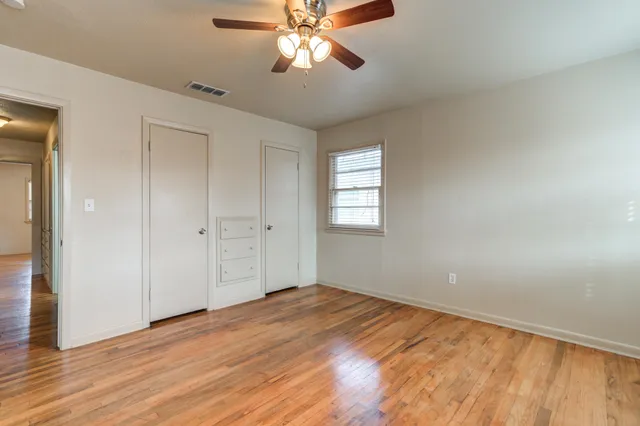 a view of empty room with wooden floor and fan