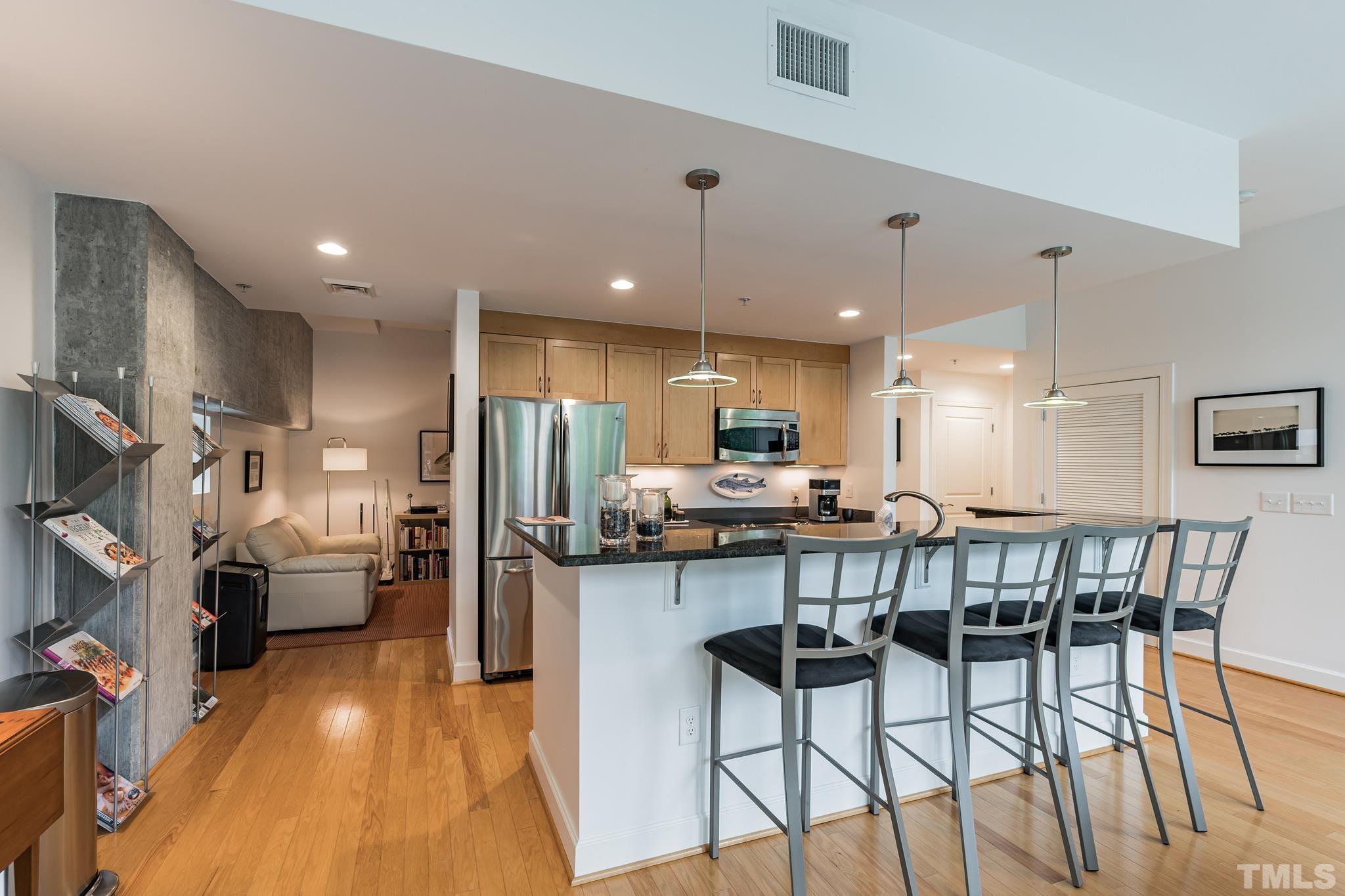 a kitchen with stainless steel appliances kitchen island granite countertop a dining table chairs and a refrigerator