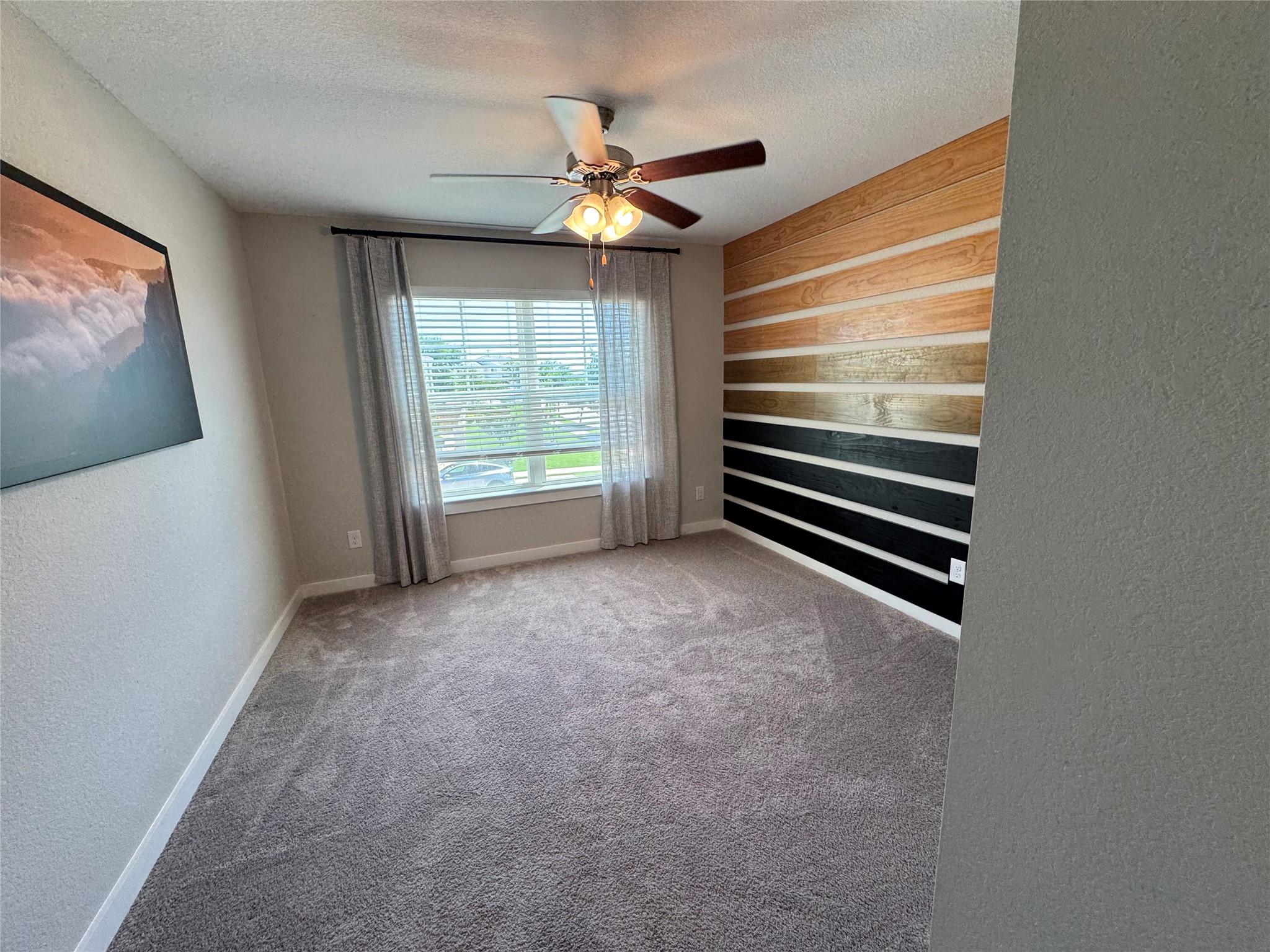 2328 Calvert Drive Leander, TX 78641 - Photo 12 of 35 Carpeted room featuring a decorative accent wall with horizontal wood planks, a multi-blade ceiling fan with integrated lighting, and a window with horizontal blinds and drapery