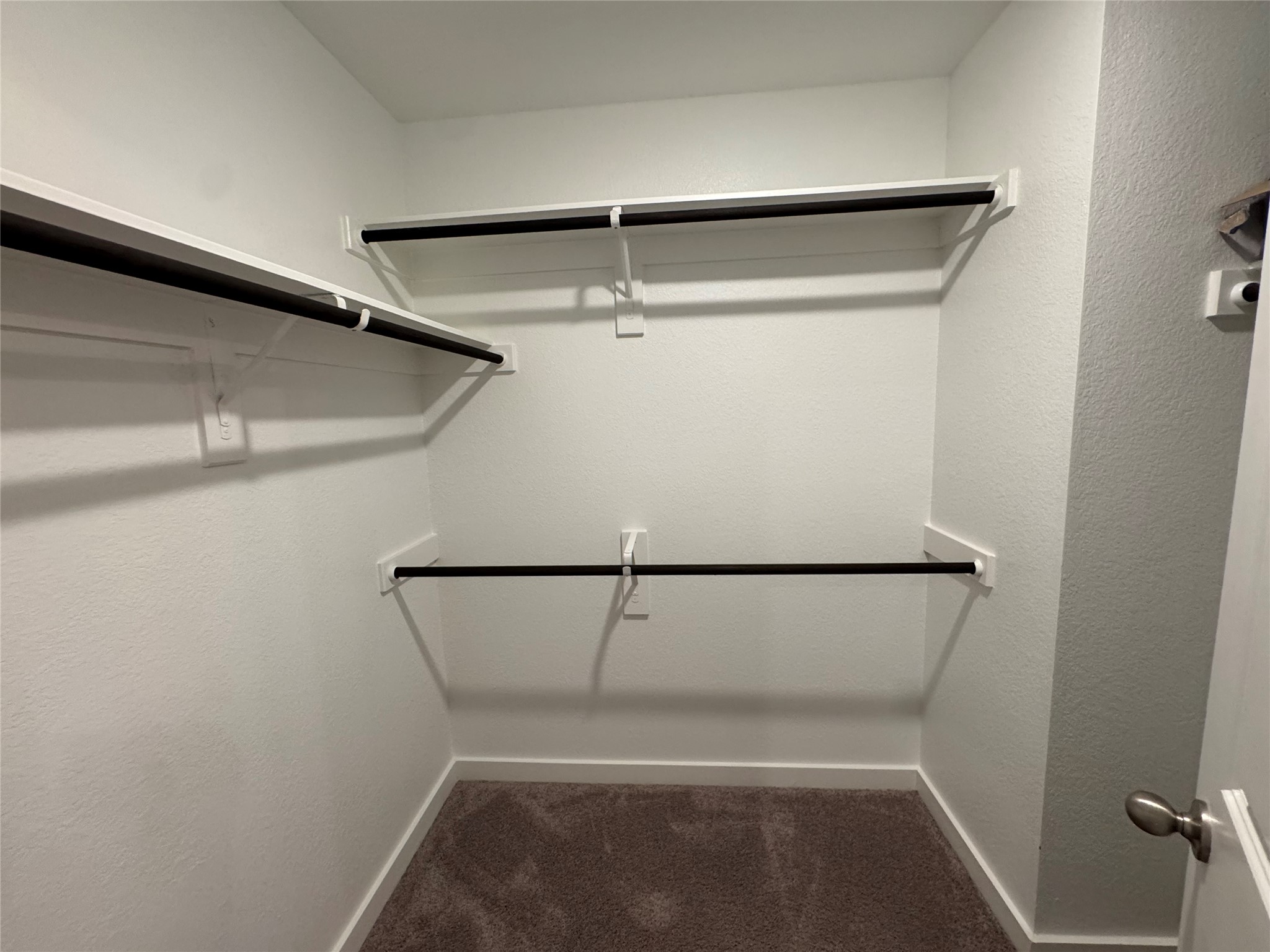 2328 Calvert Drive Leander, TX 78641 - Photo 24 of 35 Walk-in closet featuring white painted walls, textured ceiling, brown carpet flooring, and multiple built-in shelving units with black hanging rods