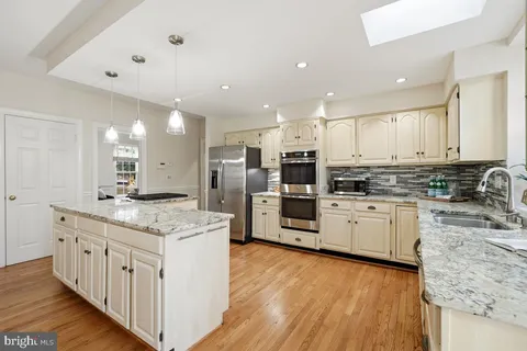 a kitchen with stainless steel appliances kitchen island granite countertop a stove a sink a refrigerator and white cabinets with wooden floor
