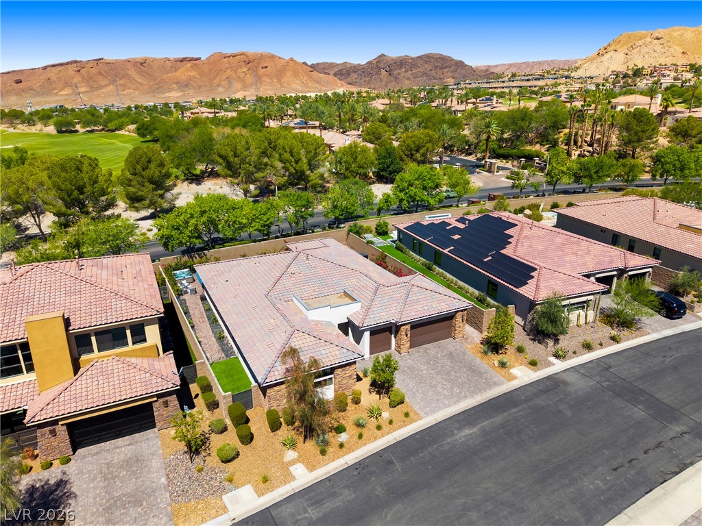 45 Garibaldi Way Henderson, NV 89011 - Photo 43 of 74 An aerial perspective reveals a desert oasis with residential rooftops, solar panels, and a golf course against a mountain backdrop.