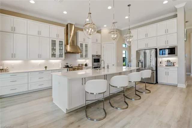 a large white kitchen with a refrigerator a stove a sink and white cabinets with wooden floor