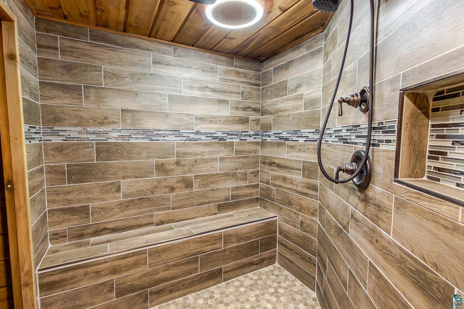 29 Ridge Road Esko, MN 55733 - Photo 31 of 41 Sitting room off sauna. Shower featuring wood-finish tile walls with a decorative mosaic band, a built-in bench, a recessed niche with mosaic tile, bronze-finish fixtures, and a pebble tile shower floor