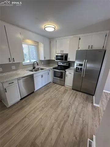 a large kitchen with a stove a sink dishwasher a refrigerator and white cabinets with wooden floor