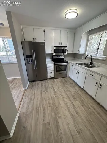 a kitchen with granite countertop a refrigerator a sink dishwasher a stove and white countertops with wooden floor