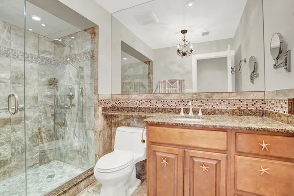 a bathroom with a granite countertop sink a toilet a mirror and shower