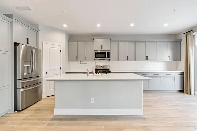 a kitchen with stainless steel appliances granite countertop a refrigerator a stove a sink and white cabinets with wooden floor