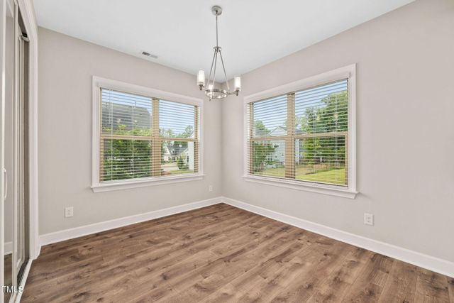 an empty room with wooden floor chandelier and windows