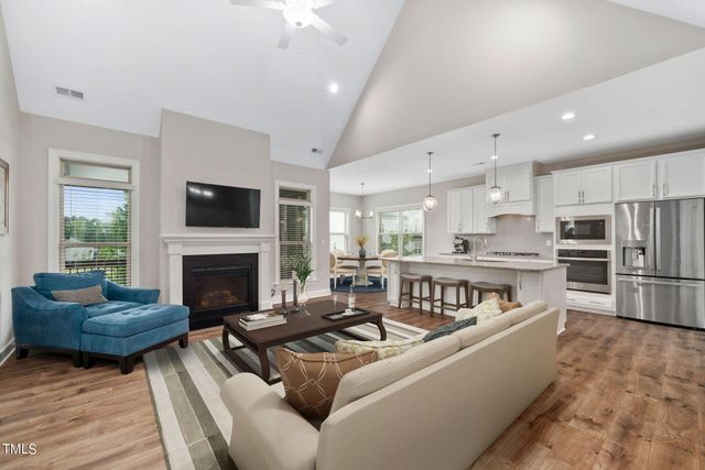 a living room with stainless steel appliances furniture a fireplace and a kitchen view