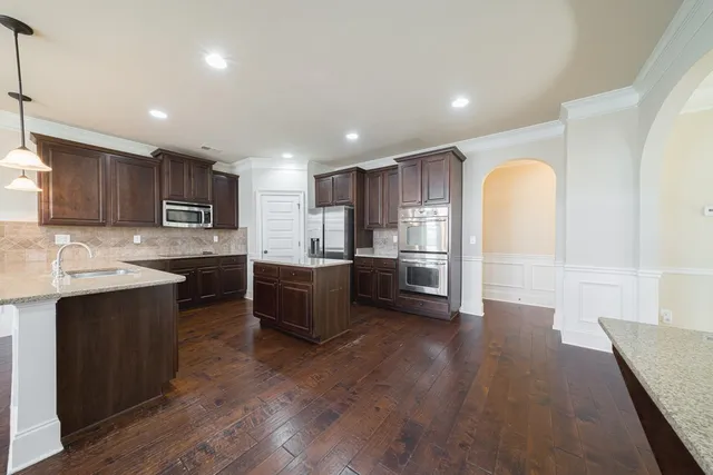 a kitchen with stainless steel appliances granite countertop a refrigerator a sink dishwasher a oven with wooden cabinets and floor