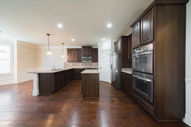 a kitchen with stainless steel appliances granite countertop a refrigerator a sink dishwasher a stove with wooden cabinets and floor