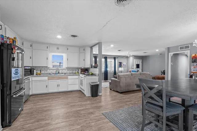 a kitchen with stainless steel appliances kitchen island granite countertop a refrigerator a stove a sink and white cabinets with wooden floor