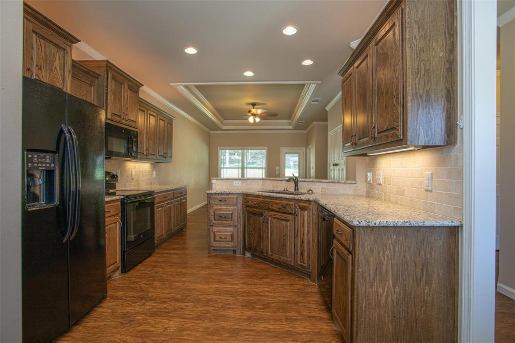 455 Neals Hill Road Oak Ridge, TX 76240 - Photo 11 of 19 Kitchen featuring black appliances, ornamental molding, light stone counters, dark wood-style floors, and backsplash