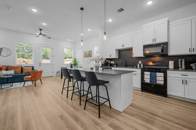 a kitchen with stainless steel appliances kitchen island granite countertop a stove a sink a microwave a dining table and chairs with wooden floor