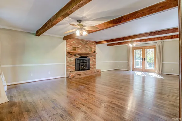 a view of an empty room with wooden floor fireplace and a window