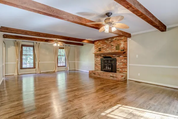 a view of an empty room with wooden floor fireplace and a window