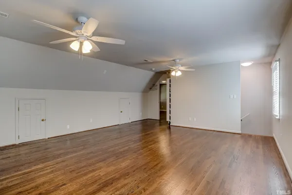 a view of an empty room with wooden floor and a ceiling fan