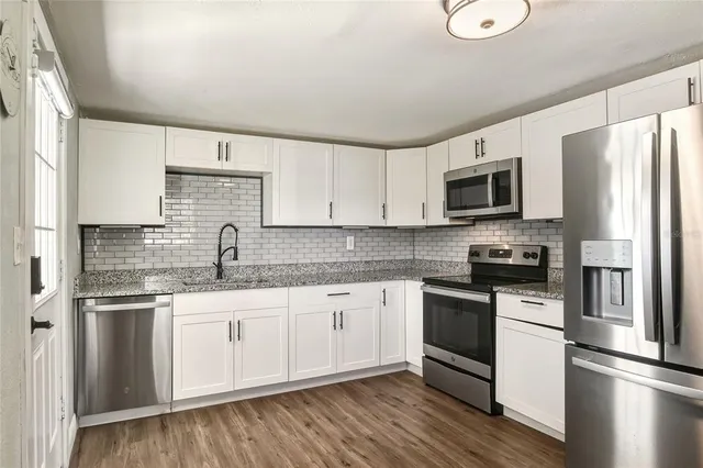 a kitchen with granite countertop a sink stainless steel appliances and white cabinets