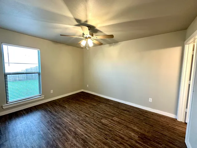an empty room with wooden floor fan and windows