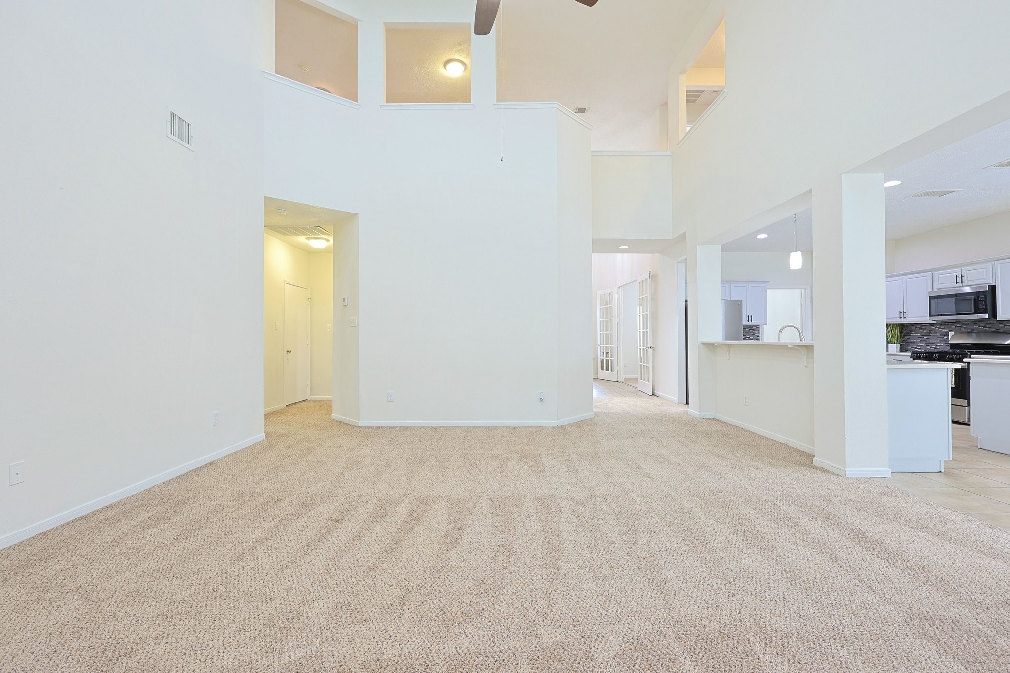 23019 Eastgate Village Drive Spring, TX 77373 - Photo 46 of 46 This spacious living area features high ceilings, neutral carpeting, and an open floor plan that seamlessly connects to a modern kitchen with white cabinetry and stainless steel appliances, creating a bright and inviting atmosphere.