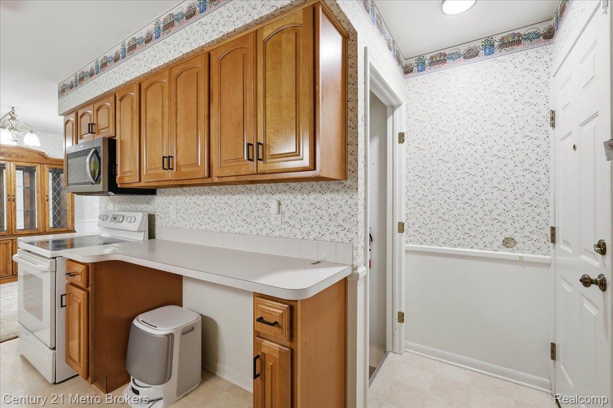 5457 North Seymour Road Flushing, MI 48433 - Photo 22 of 43 Kitchen featuring wood finish cabinetry, wallpapered walls, white electric range oven, light flooring, and light countertops