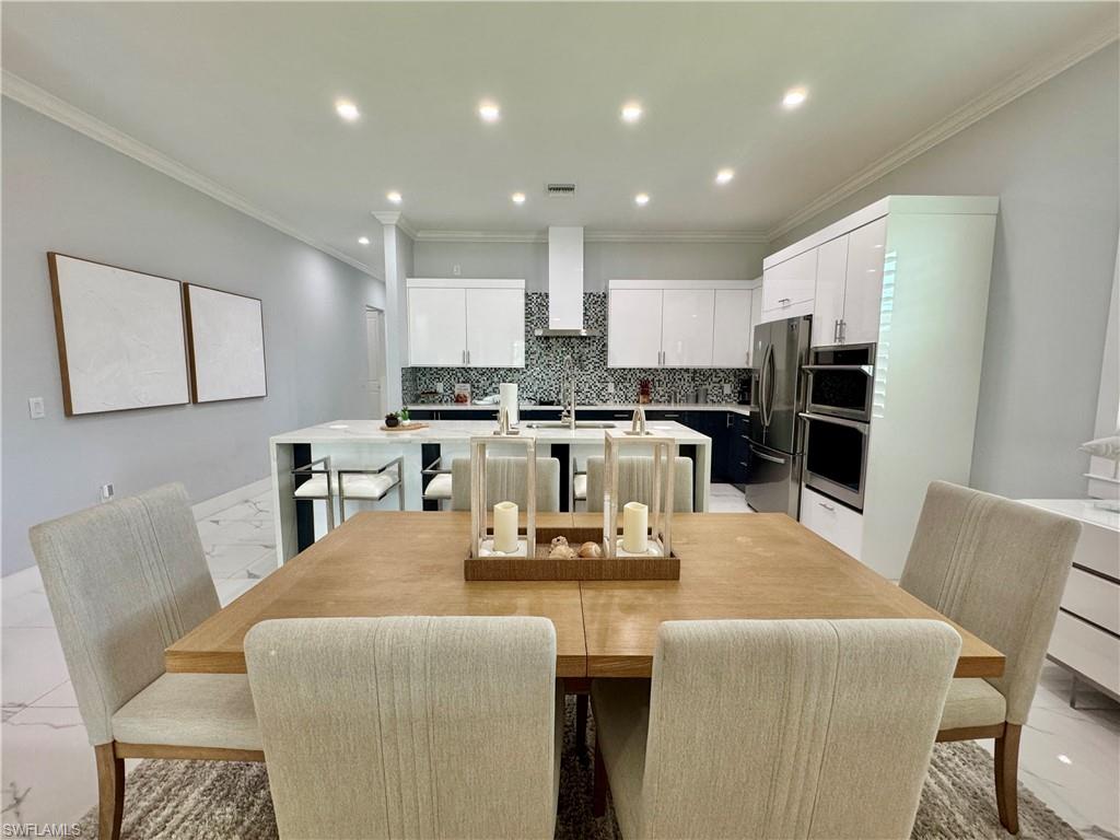656 108th Avenue North Naples, FL 34108 - Photo 10 of 48 Kitchen featuring a kitchen island with sink, light stone countertops, stainless steel fridge, a kitchen bar, and wall chimney exhaust hood