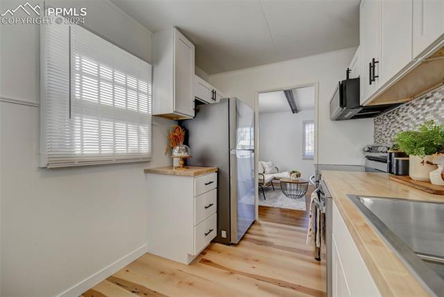 507 East Cheyenne Road Colorado Springs, CO 80905 - Photo 20 of 25 Kitchen with light wood-type flooring, crown molding, wooden counters, appliances with stainless steel finishes, and white cabinets