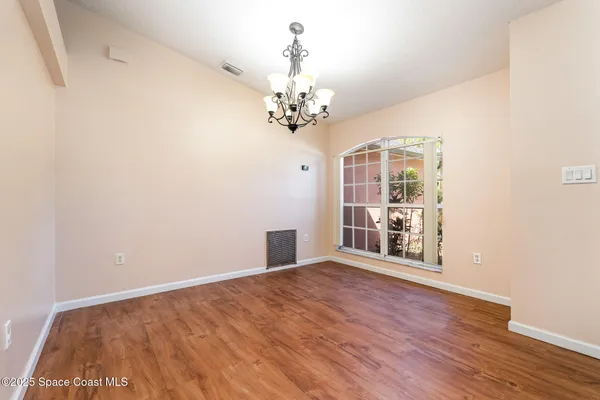 an empty room with wooden floor chandelier and windows