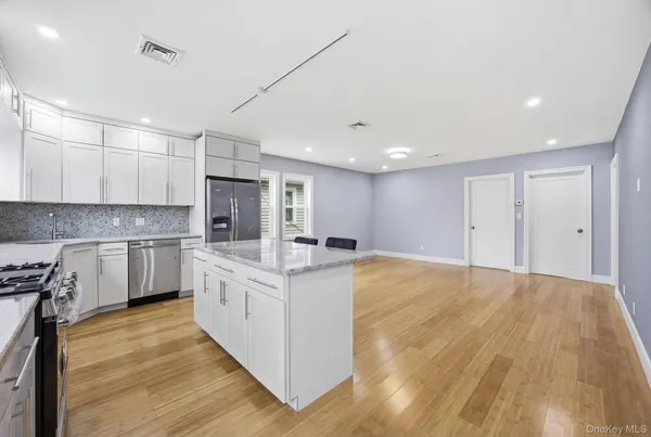 a large kitchen with kitchen island a stove a sink dishwasher a refrigerator and white cabinets with wooden floor