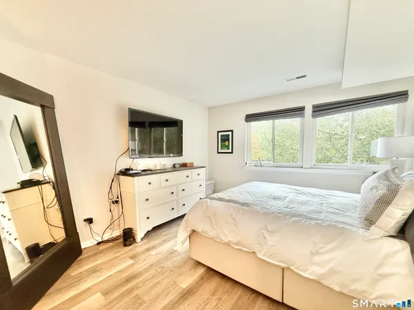 a bedroom with a bed and a flat tv screen on dresser next to a window