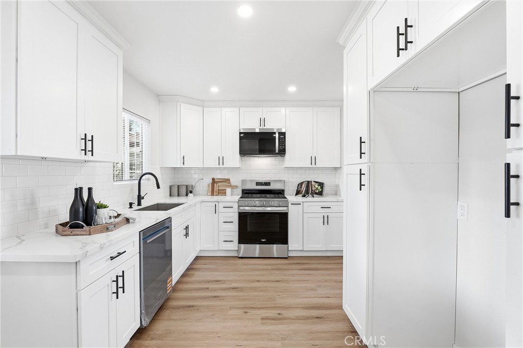 2835 Delta Avenue Long Beach, CA 90810 - Photo 11 of 29 a kitchen with stainless steel appliances granite countertop a stove top oven a sink a refrigerator and white cabinets with wooden floor