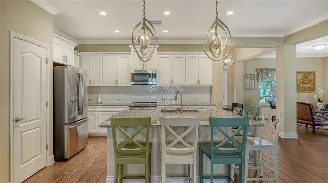 a kitchen with stainless steel appliances a dining table chairs a refrigerator and cabinets