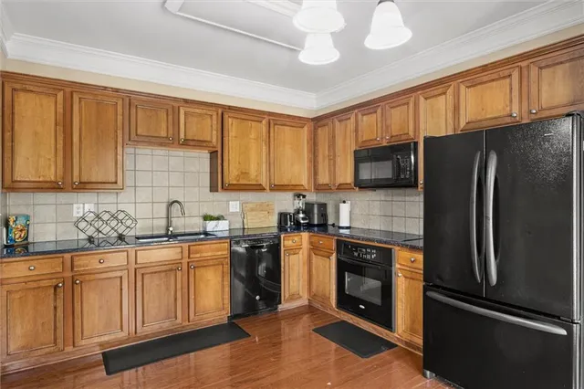 a kitchen with stainless steel appliances granite countertop a refrigerator a sink dishwasher a stove top oven a kitchen island and chairs with wooden floor