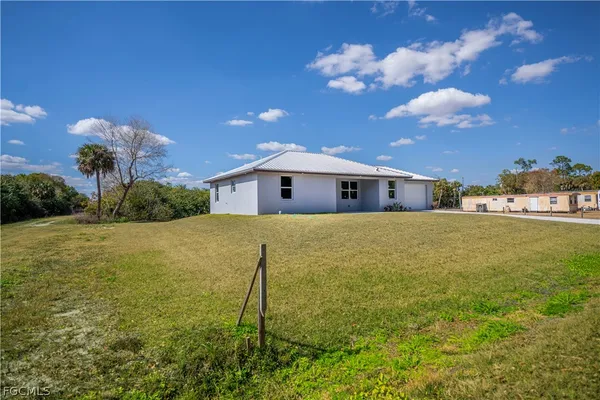 a white house with a big yard plants and large trees