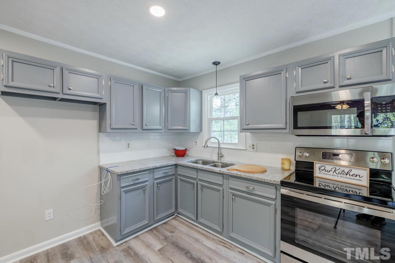 6803 Russell Road Durham, NC 27712 - Photo 12 of 27 a kitchen with stainless steel appliances granite countertop a sink dishwasher stove and white cabinets with wooden floor