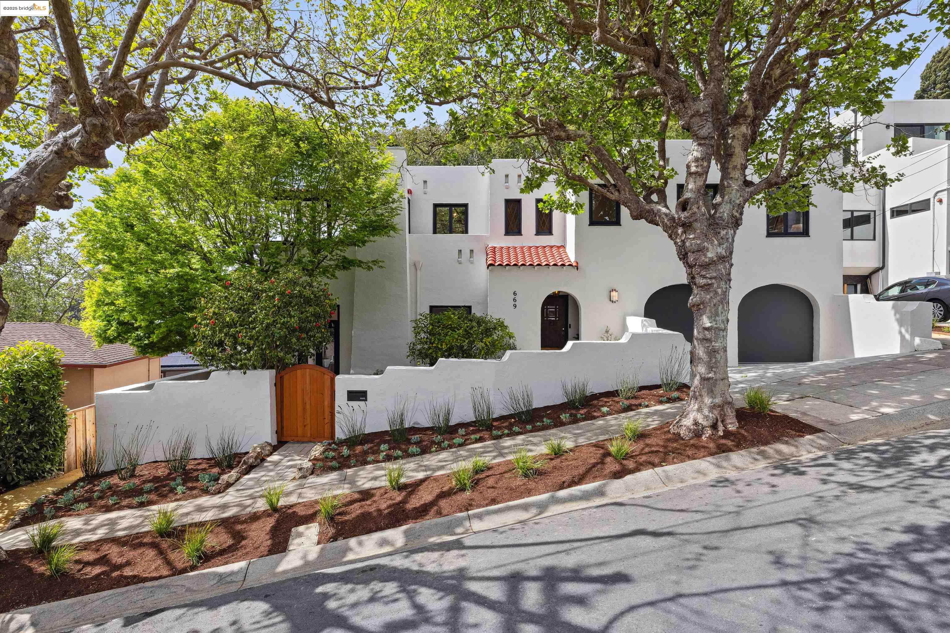 a view of a white house with a large tree and wooden fence