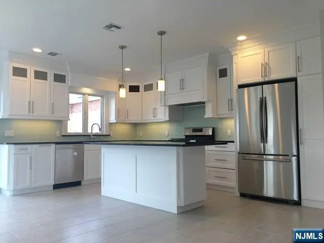 a kitchen with stainless steel appliances granite countertop a refrigerator a sink and white cabinets