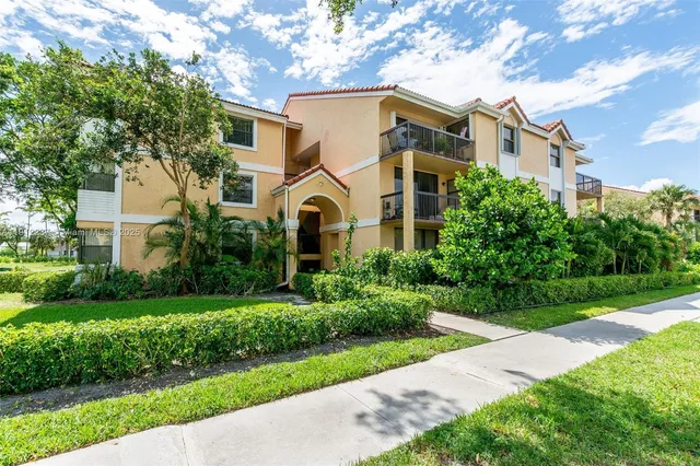 a view of a white house with a big yard plants and large trees