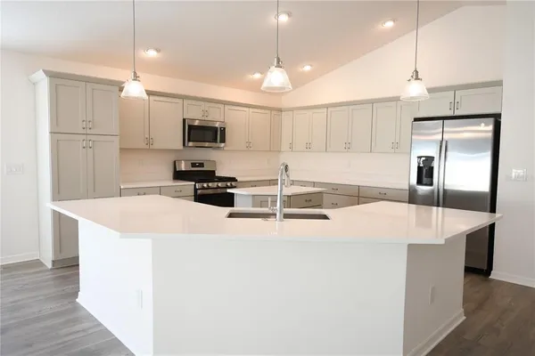 a large kitchen with kitchen island a stove a sink a refrigerator and white cabinets with wooden floor