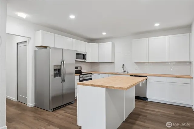 a kitchen with stainless steel appliances granite countertop a refrigerator a sink dishwasher a stove top oven a refrigerator and white cabinets with wooden floor