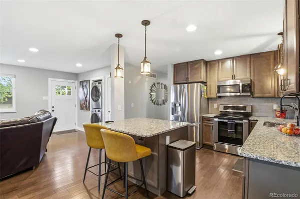 a kitchen with stainless steel appliances granite countertop a sink a stove a refrigerator cabinets and chairs