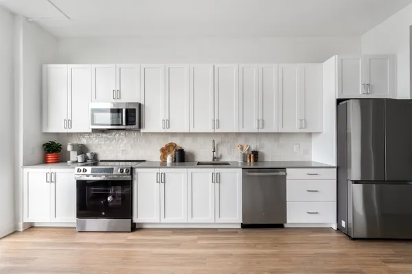 a kitchen with stainless steel appliances granite countertop a refrigerator stove a sink and white cabinets with wooden floor