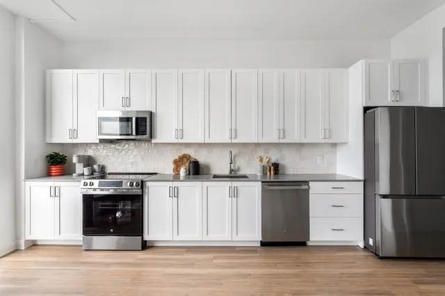 a kitchen with stainless steel appliances granite countertop a refrigerator stove a sink and white cabinets with wooden floor