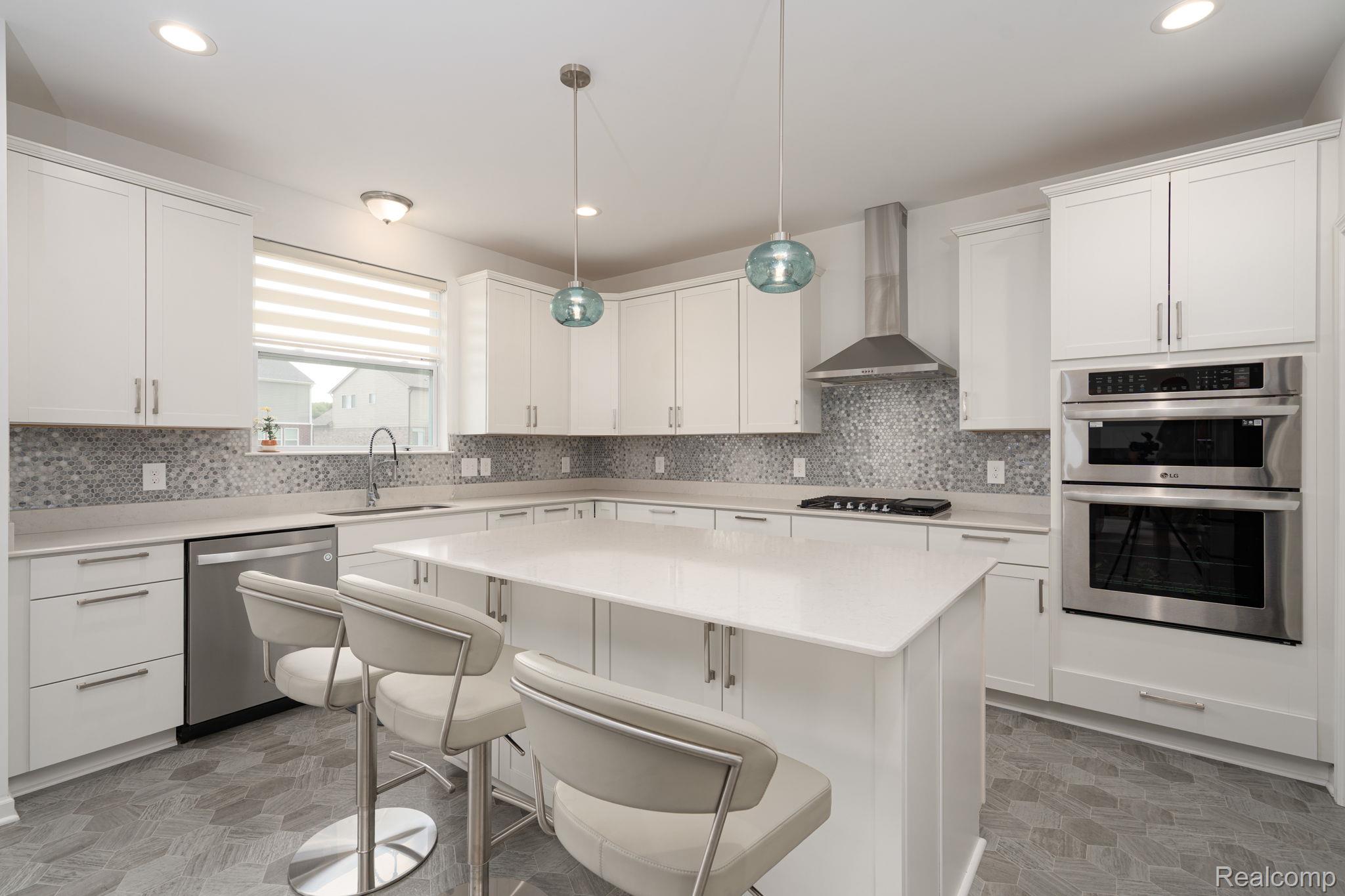 48904 Carnegie Way Macomb, MI 48042 - Photo 8 of 34 Spacious kitchen featuring white cabinetry, quartz countertops, a mosaic tile backsplash, stainless steel appliances including a wall oven and microwave, and hexagon-patterned floor tiling